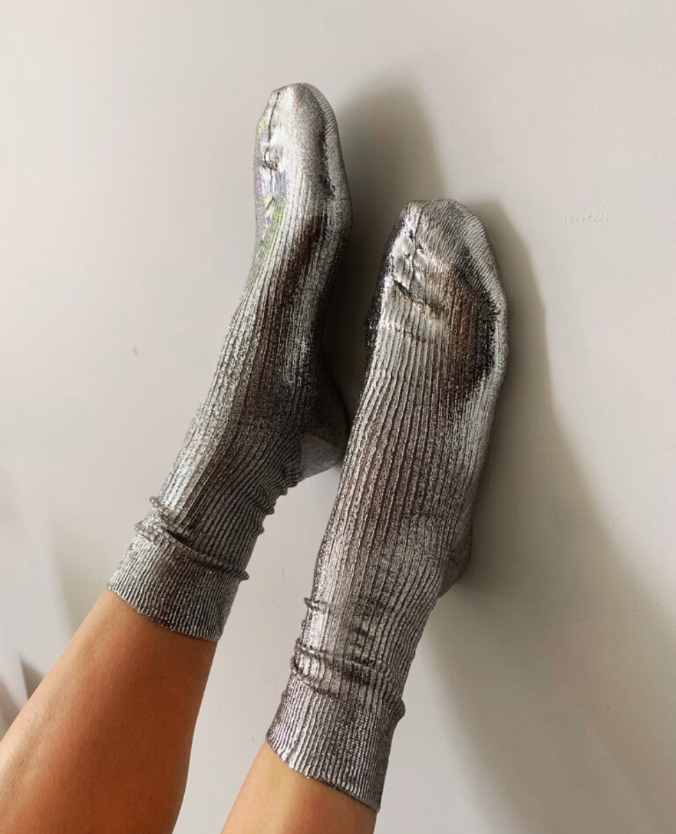 Shiny silver socks with a ribbed texture, mid-calf length, and a snug fit, made from a metallic, stretchy fabric.