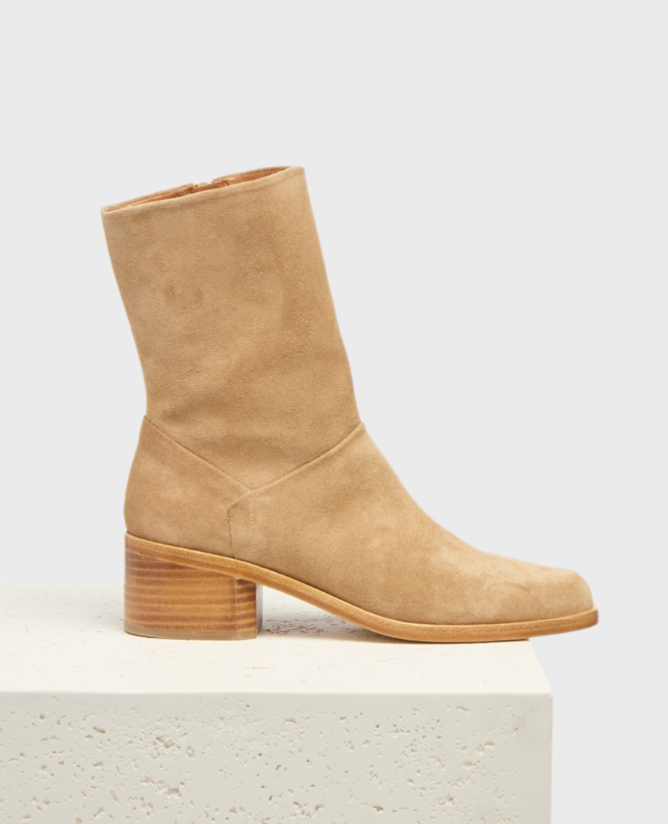 A tan suede ankle boot with a smooth texture, featuring a mid-height wooden block heel and a sleek, minimalist design.