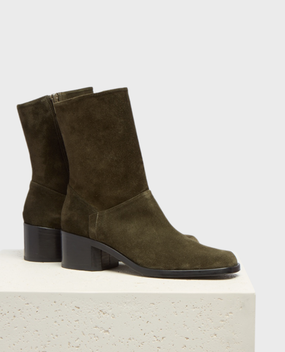 Olive green suede ankle boots with a square toe, mid-height block heel, and side zipper, featuring a smooth, matte texture and a sleek, minimalist design.