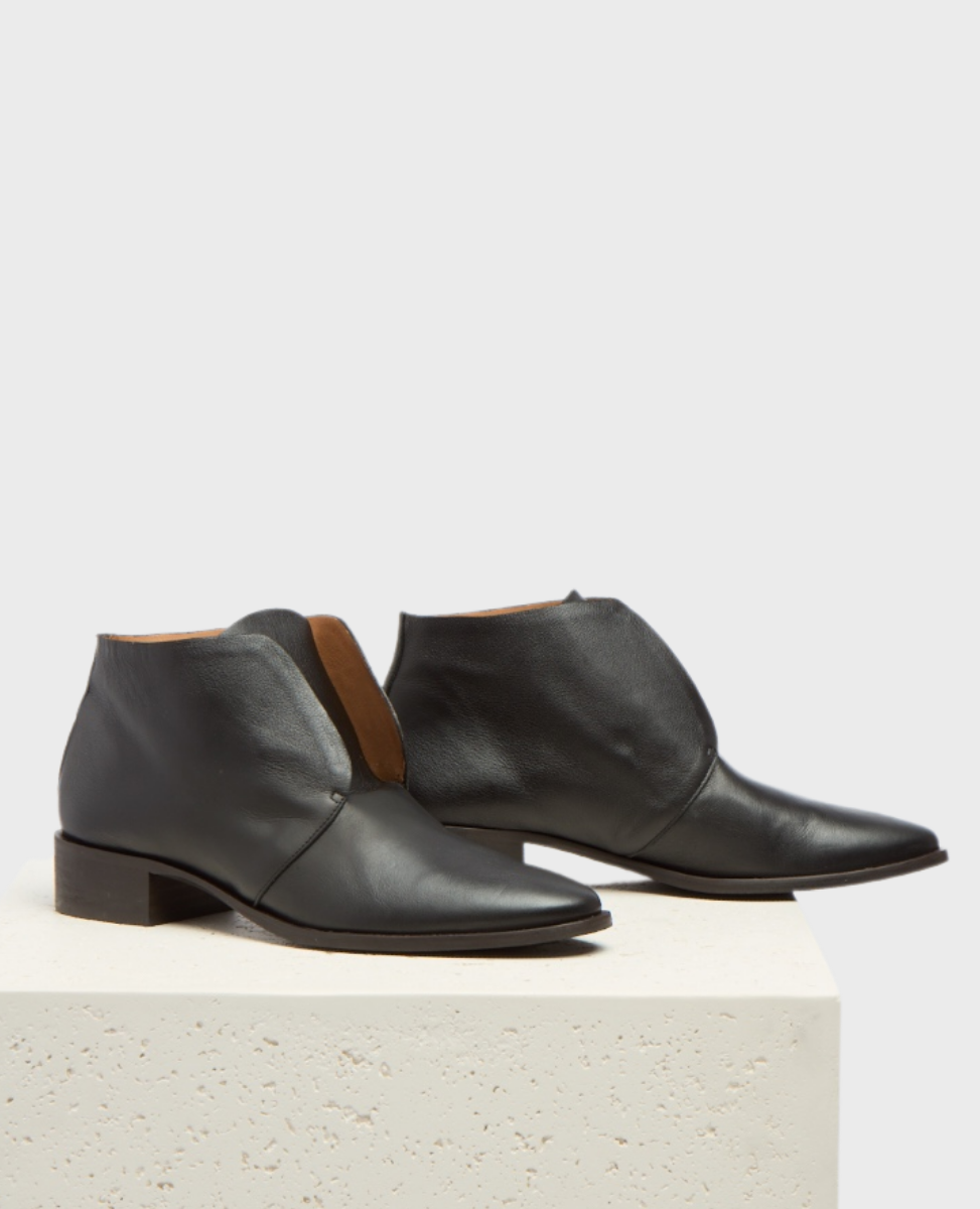 Sleek black leather ankle boots with a pointed toe, low stacked heel, and a smooth, polished finish, featuring a minimalist design with a subtle side seam.