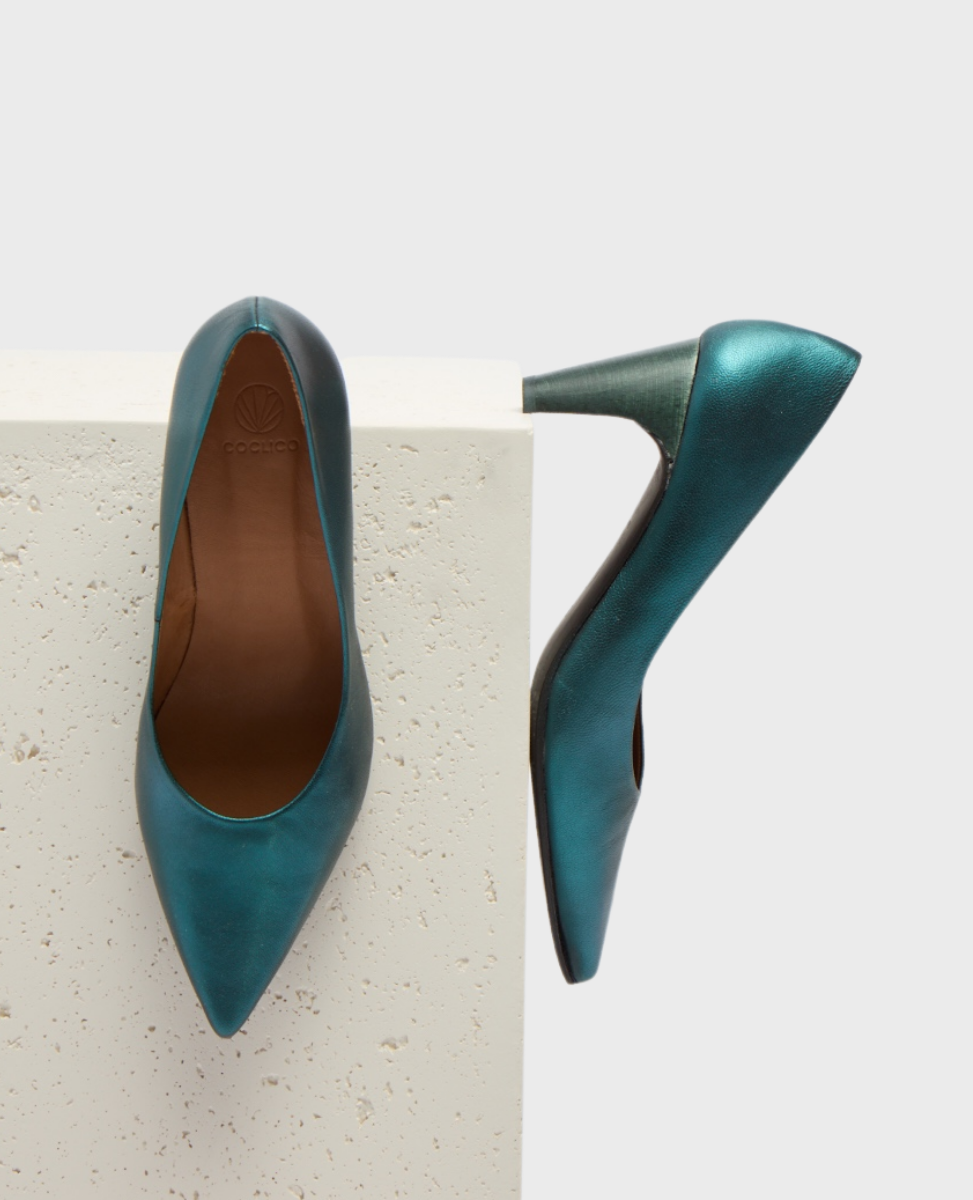 A pair of elegant, metallic teal high-heeled shoes with a pointed toe, smooth leather texture, and a sleek, glossy finish, featuring a stiletto heel and a subtle logo embossed on the insole.
