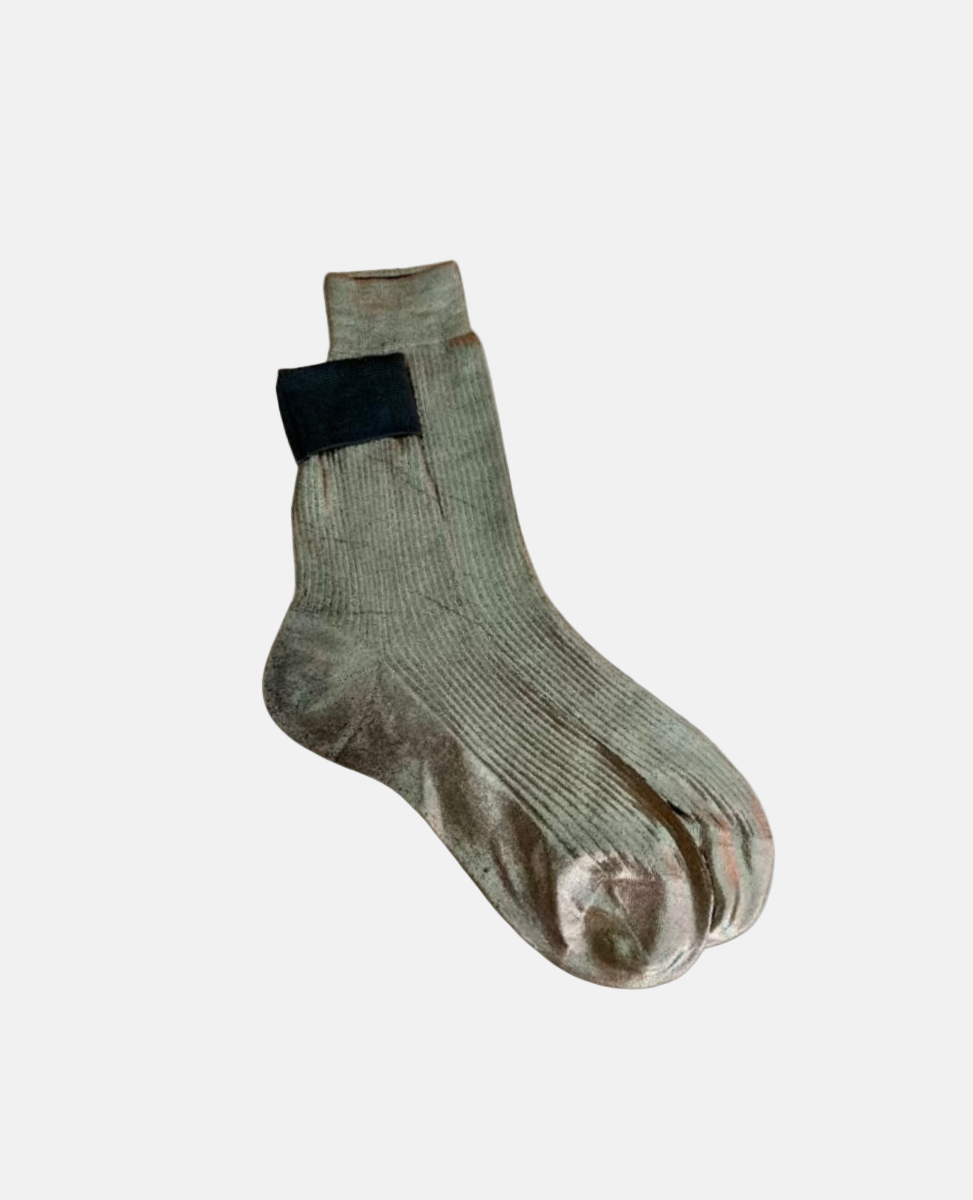 A pair of light gray, mid-calf socks with a ribbed texture, featuring a black rectangular patch near the top.