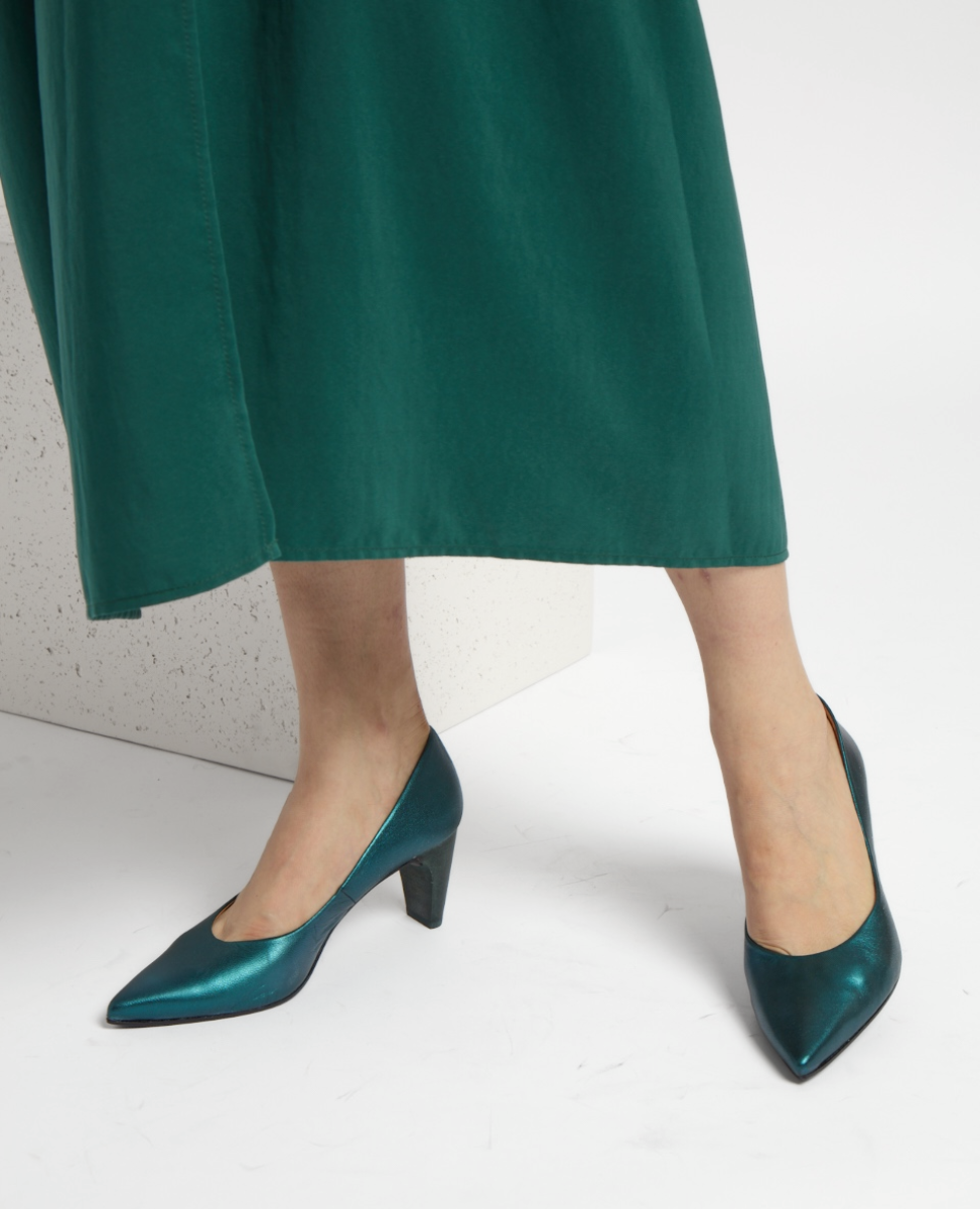 A pair of elegant, teal-colored high-heeled shoes with a pointed toe design, smooth leather texture, and a medium-height block heel, worn with a matching green dress.