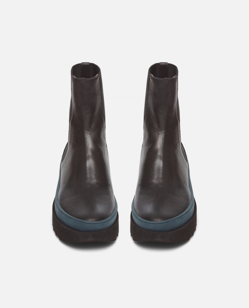 Pair of dark brown ankle boots with blue soles on a light gray background