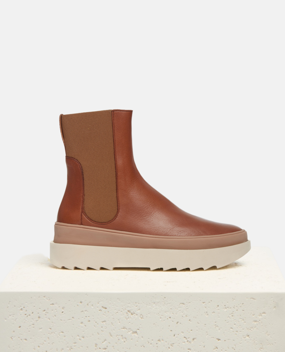 Brown ankle boot with white sole on a light beige background