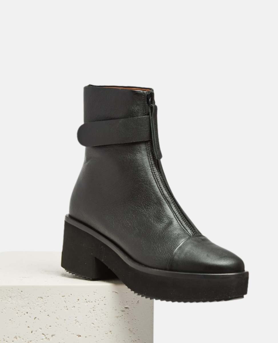 Black leather boot with a strap on a light gray background