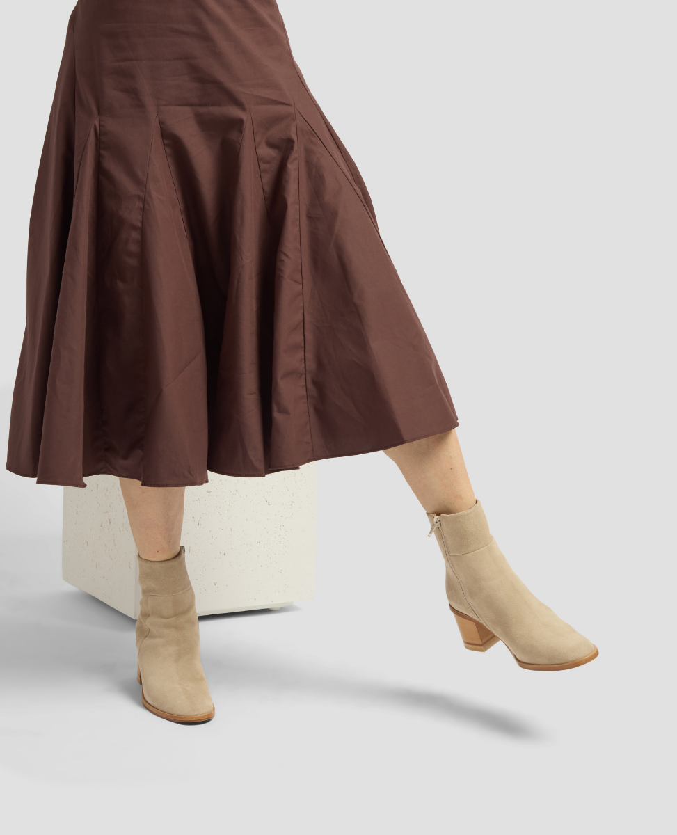 Person wearing a brown skirt and beige ankle boots on a light gray background