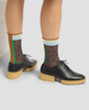 Person wearing black shoes with brown soles and patterned socks on a light background 2