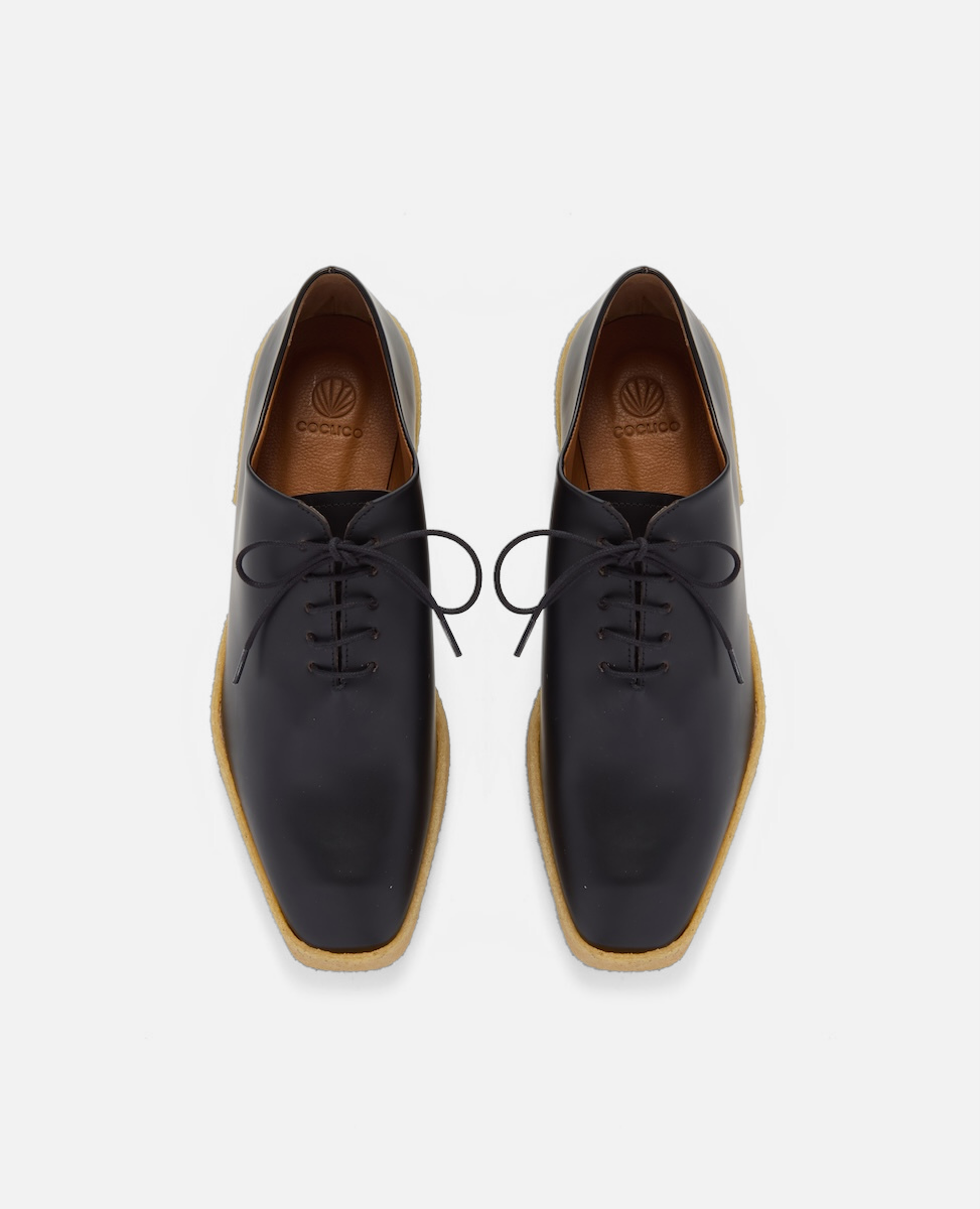 Pair of black leather shoes with wooden soles on a white background