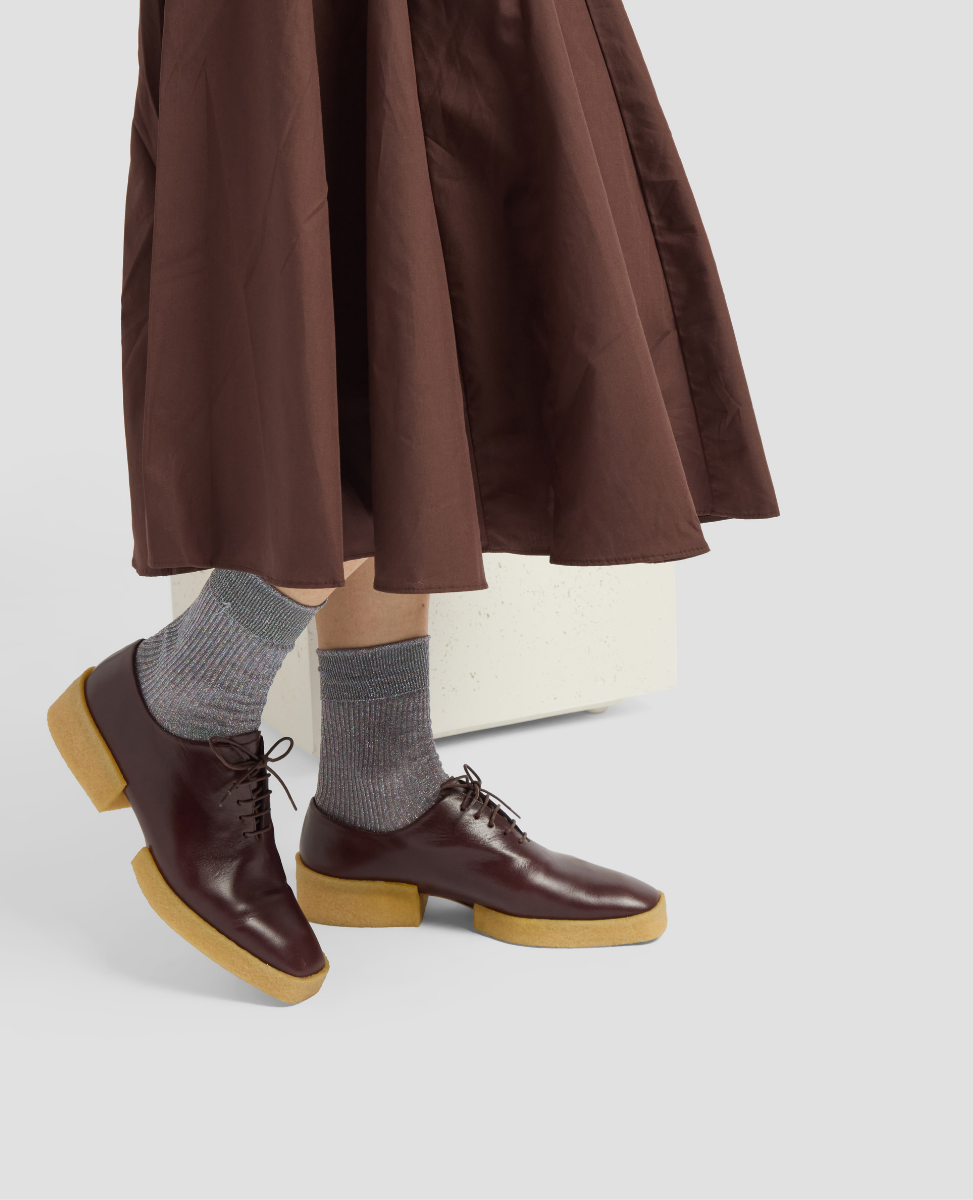 Brown shoes with beige soles worn with gray socks on a white background