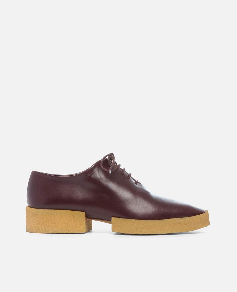 Brown leather shoe with a wooden sole on a light gray background