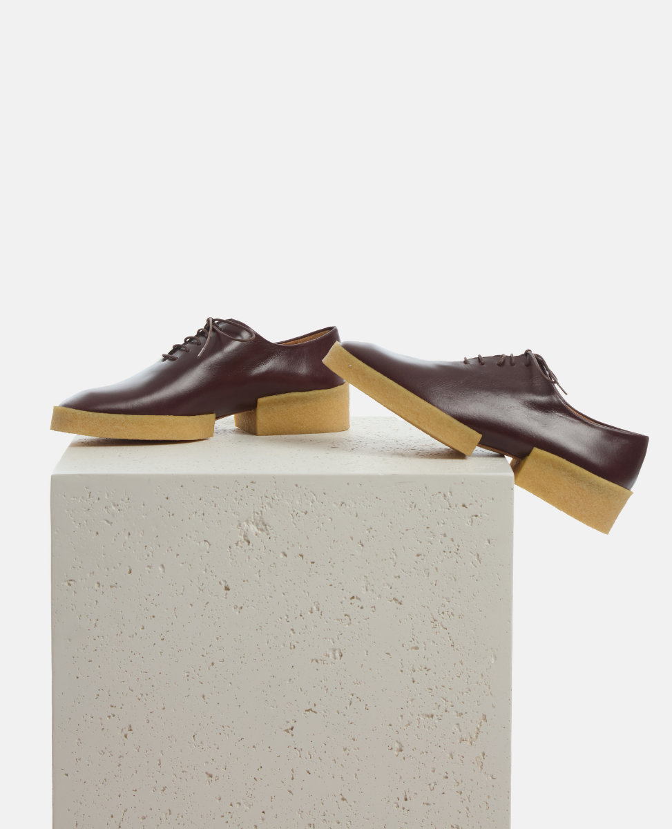 Pair of brown leather shoes with tan soles on a white pedestal