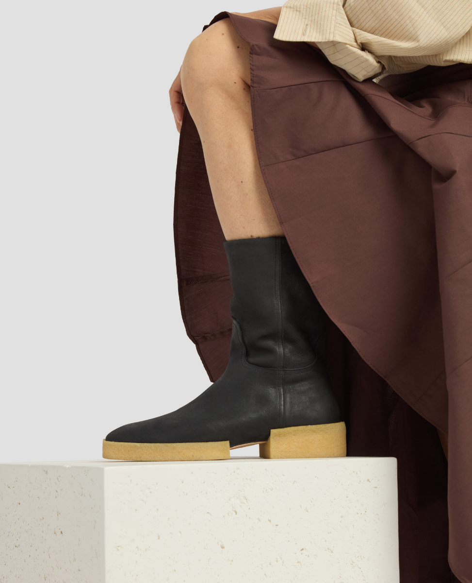 Person wearing black leather boots with wooden soles on a white platform.