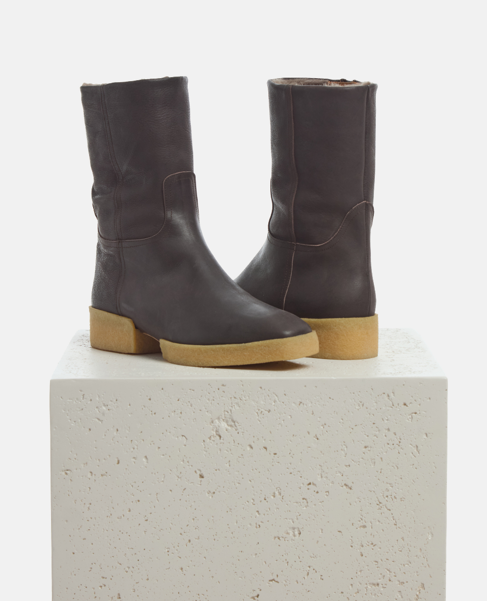 Pair of dark brown leather boots with light brown soles on a white platform.