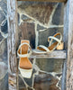 The Sterling wood heeled, strappy sandal in champagne metallic suede, perched on a ladder 2
