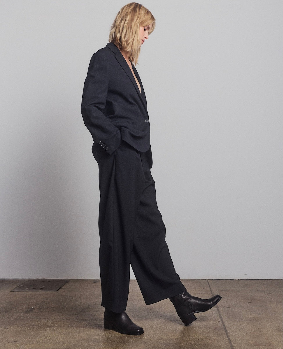 Person wearing a black suit and boots against a plain background