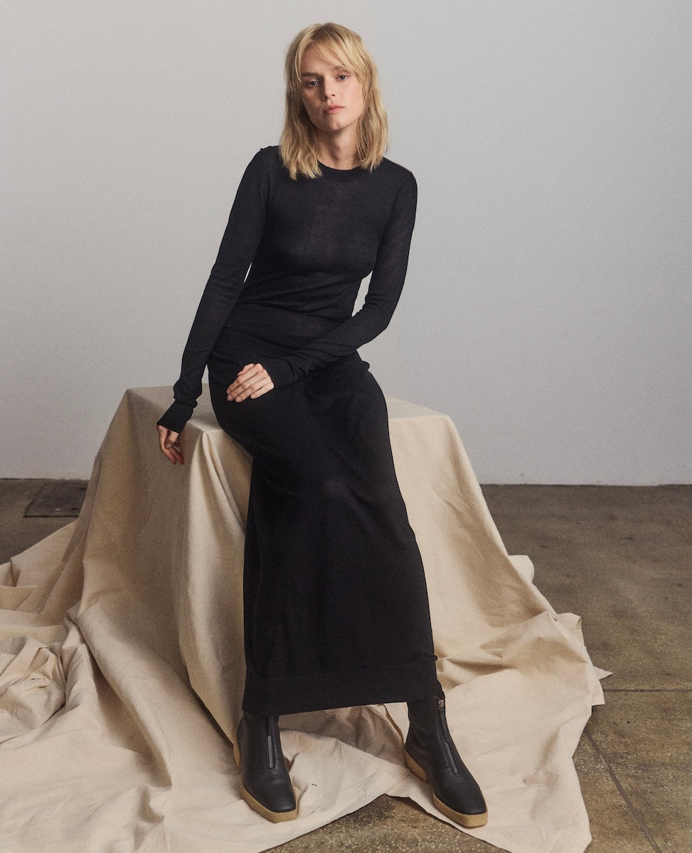 Woman wearing a black outfit sitting on a draped fabric against a plain background