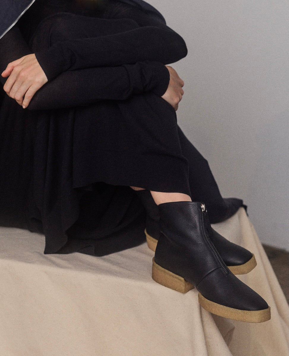 Person wearing black front-zip crepe sole
ankle boots with a neutral background
