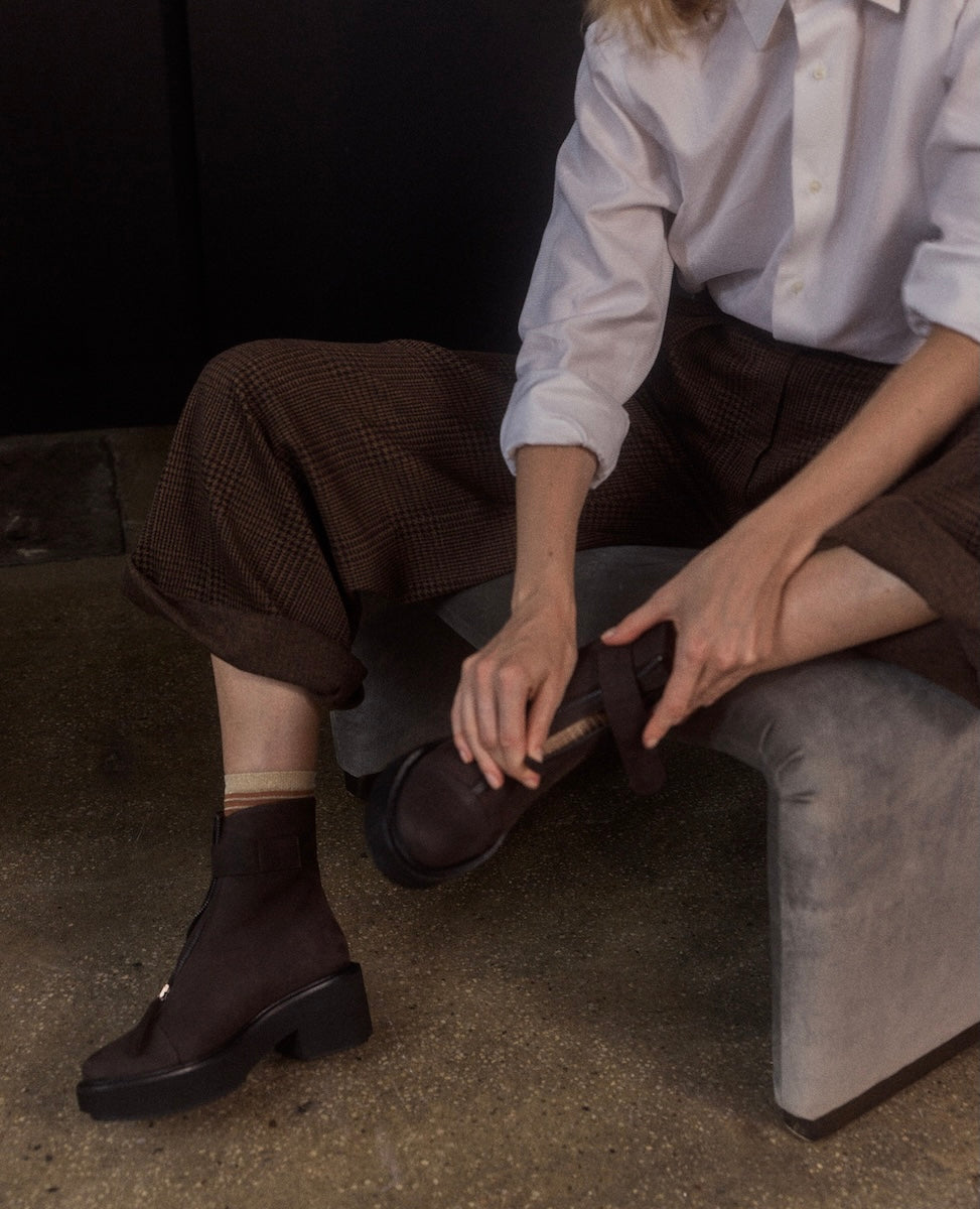 Person wearing dark brown shoes sitting on a gray surface.