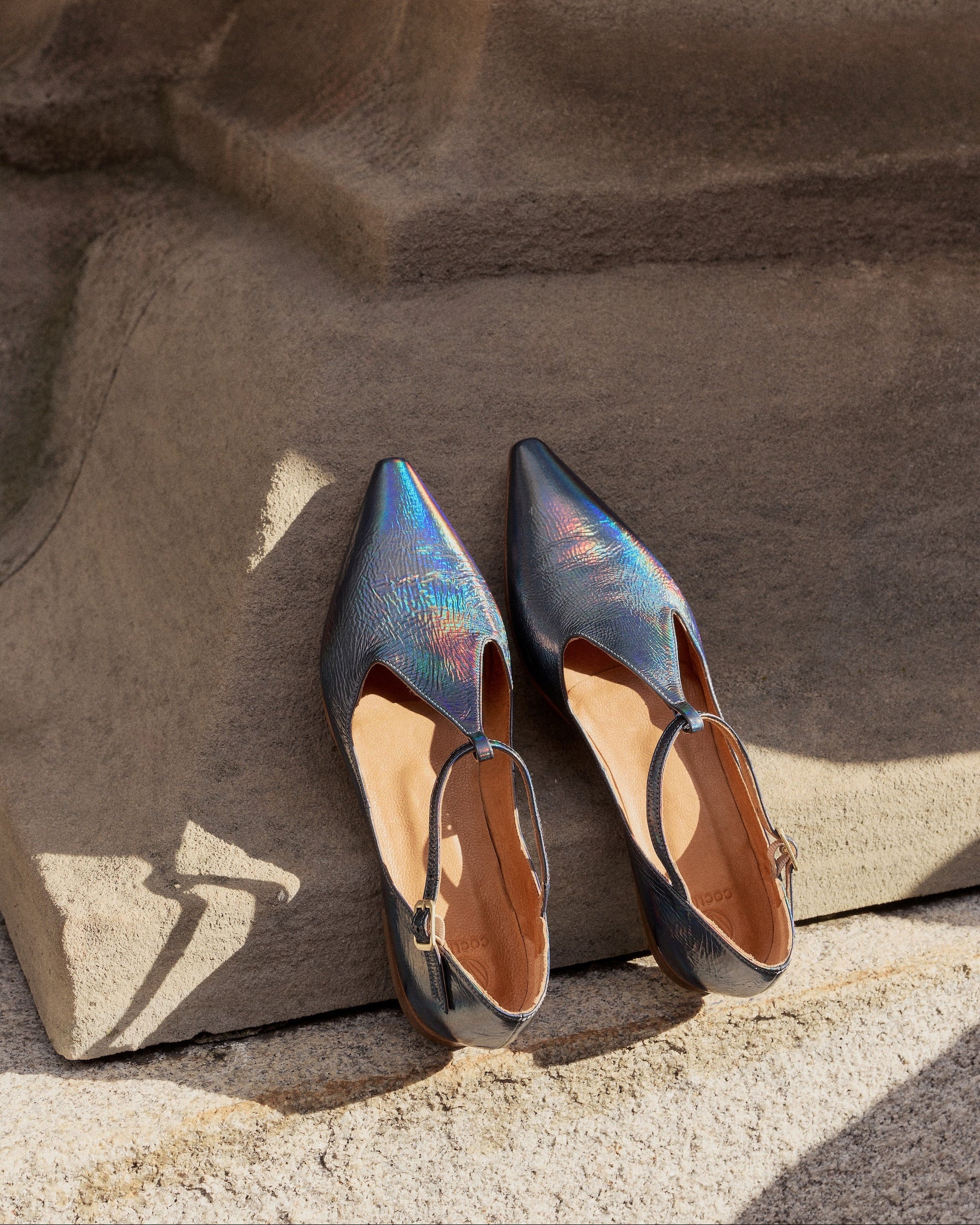 Pair of iridescent high-heeled shoes on a stone surface