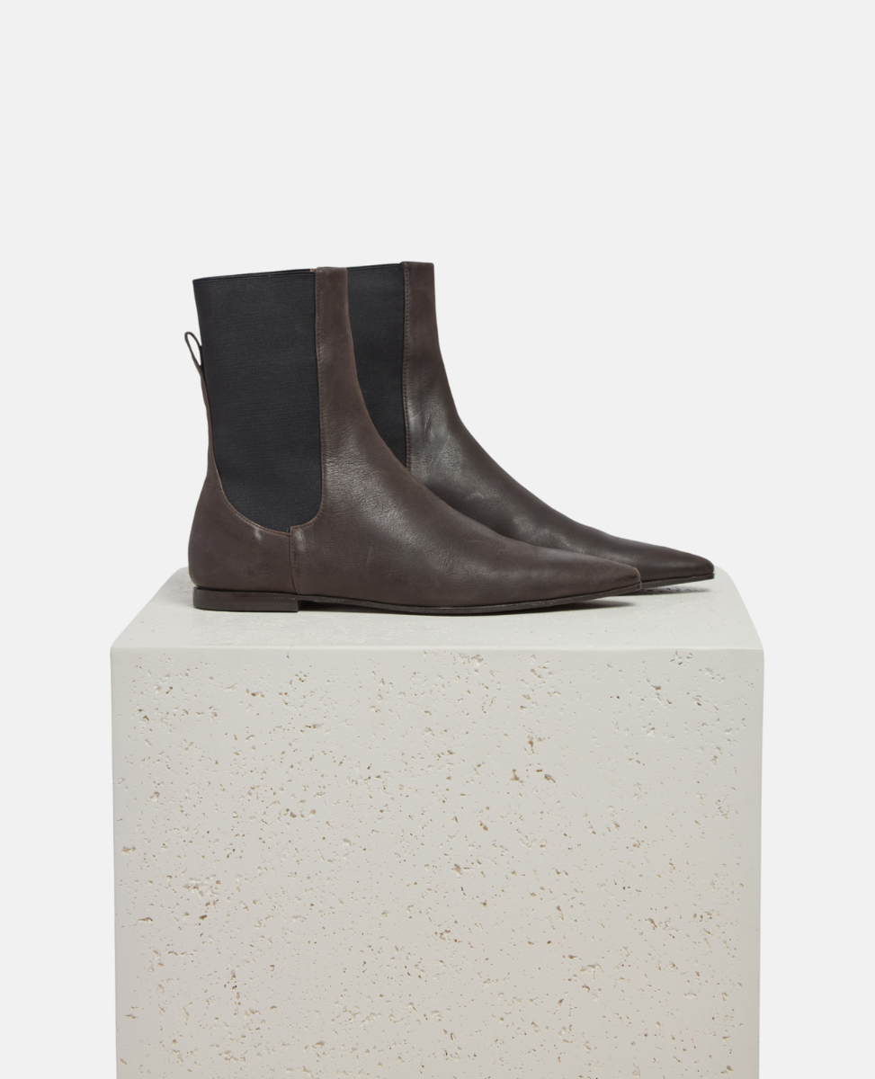 Pair of dark brown leather Chelsea boots on a light gray pedestal against a white background