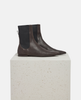 Pair of dark brown leather Chelsea boots on a light gray pedestal against a white background 4