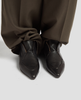 Black leather shoes worn with brown pants on a light gray background 4