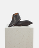 Pair of black pointed-toe shoes on a light gray pedestal against a white background 1