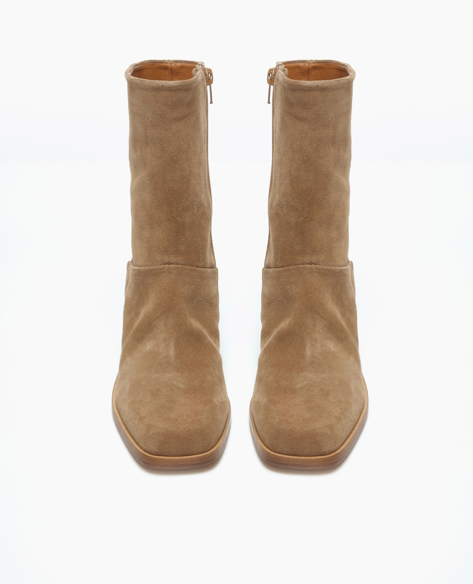 A pair of tan suede ankle boots with a smooth texture, square toes, and side zippers, featuring a minimalist design and a medium-height stacked heel.