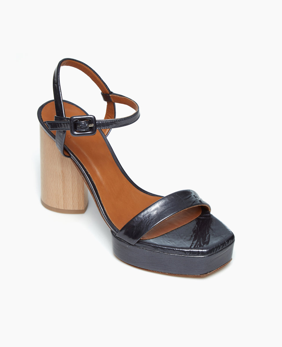 Angled view of the Angel Platform in black pearl patent leather. The heel is carved from solid ash wood, while the platform is made from lightweight, leather-covered, recycled cork.