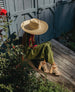 Woman sitting next to a garden wearing a straw hat, green jumpsuit and the April Heel in Latte Machiatto.  8