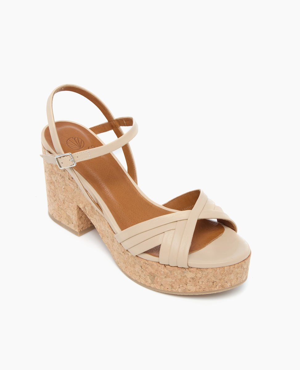 A beige sandal with a cork platform heel features crisscrossing straps at the toe, a single ankle strap, and a smooth, matte finish.