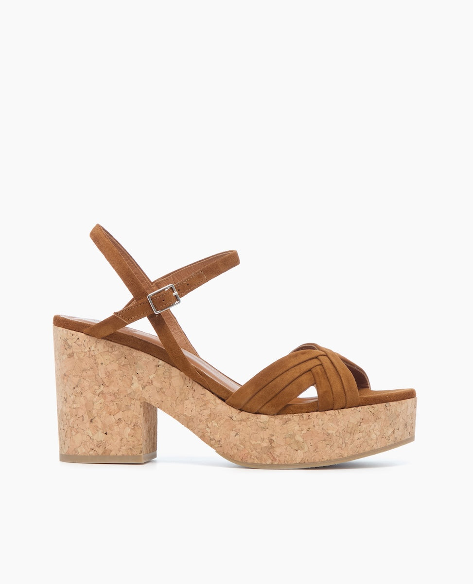 A brown suede sandal with a cork block heel, featuring a crisscross strap design and an adjustable ankle strap.