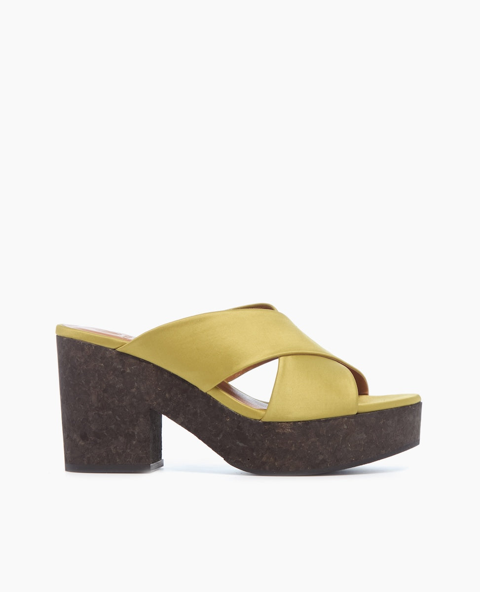 A stylish sandal featuring a mustard yellow crisscross strap design, a chunky dark brown cork platform heel, and an open toe.