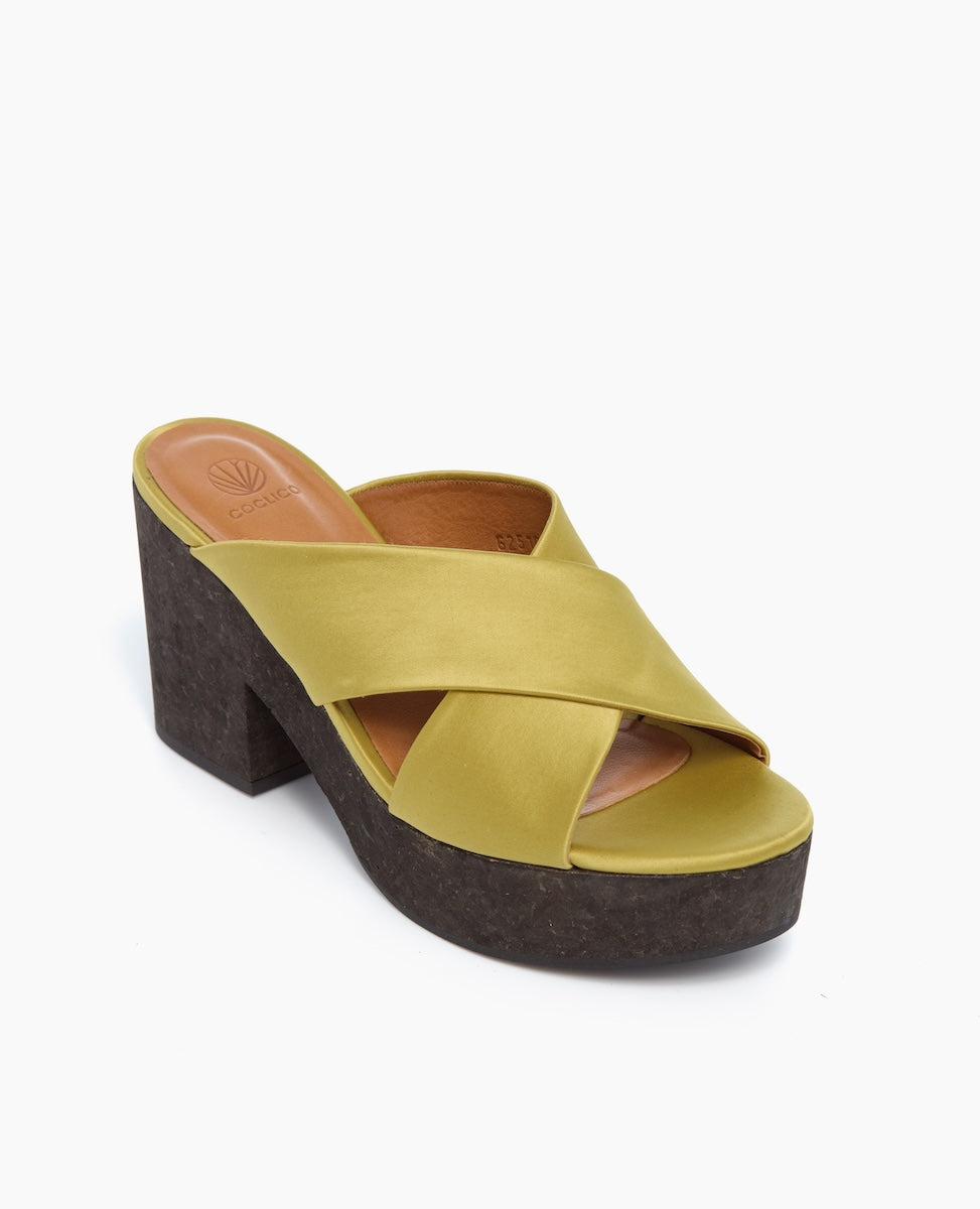 A stylish sandal featuring a mustard yellow leather upper with crisscross straps, a brown cushioned insole, and a chunky dark brown cork platform heel.