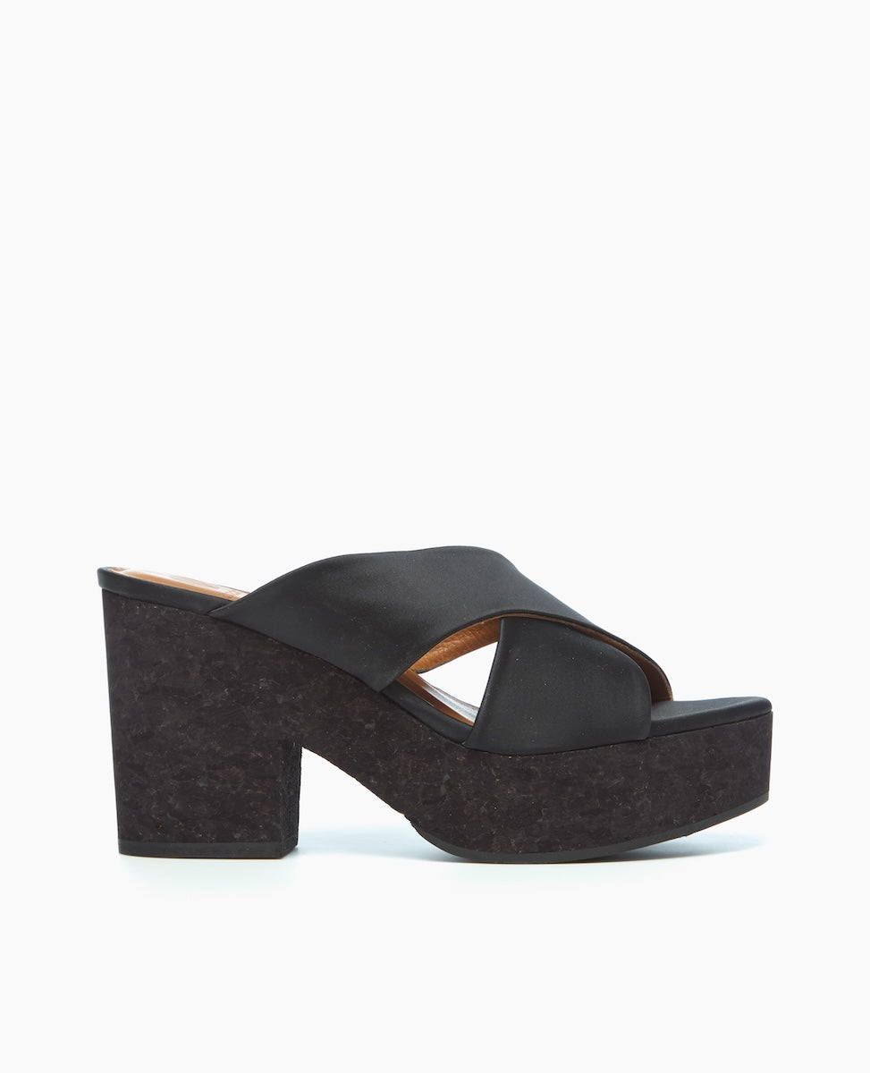 A black platform sandal featuring a thick, textured sole and heel, with a wide, smooth strap crossing over the top, creating an open-toe design.