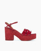 A vibrant red platform sandal features a glossy finish with a chunky heel, an open toe design, and a buckle strap, showcasing a textured sole and sleek leather straps. 2