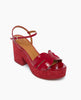 A vibrant red platform sandal features a glossy finish, a chunky heel, a crisscross strap design with a buckle closure, and a smooth, tan insole. 3