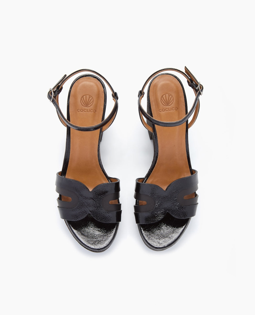 Black open-toe sandals with a smooth leather finish, featuring a wavy strap design, adjustable ankle straps with buckles, and a tan insole with a logo imprint.