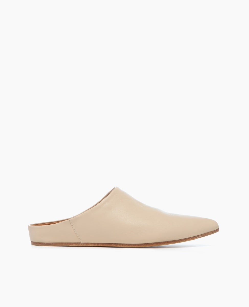 A minimalist beige leather mule with a smooth texture, featuring a closed pointed toe, a flat sole, and a slip-on design.