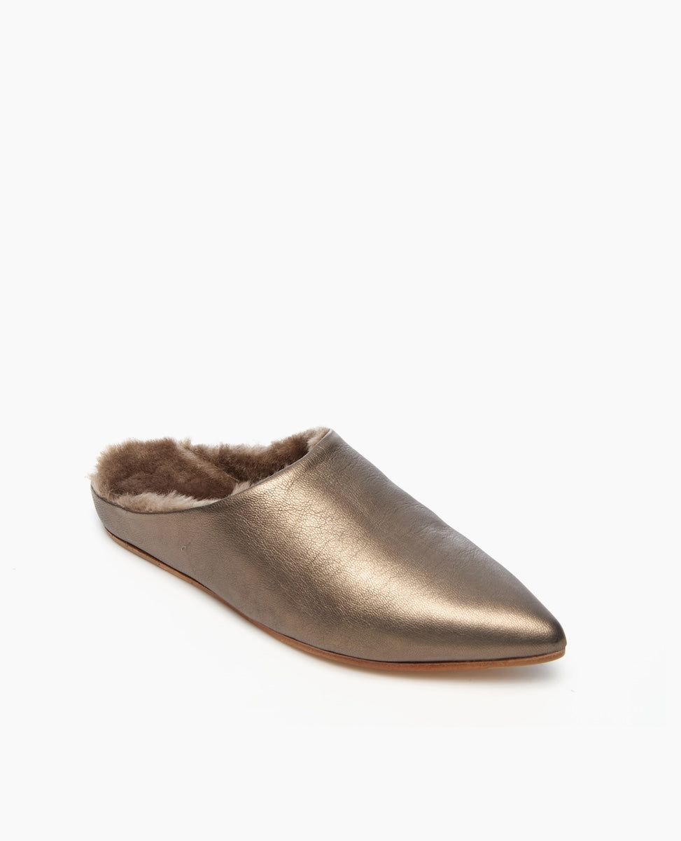 A sleek, metallic bronze mule slipper with a pointed toe, featuring a plush, brown faux fur lining and a flat sole.