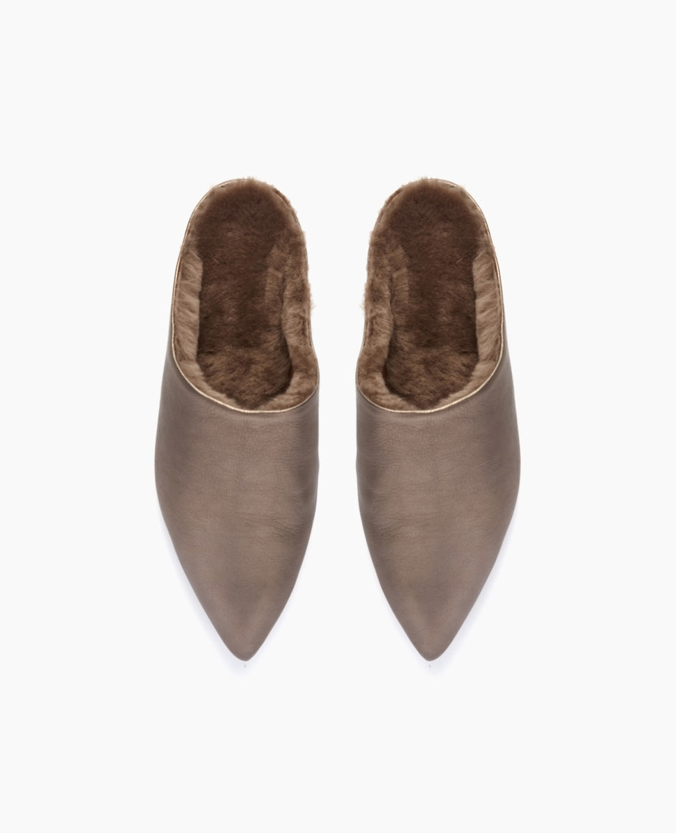 Taupe-colored, pointed-toe slippers with a plush, brown faux fur lining, featuring a smooth leather-like exterior and a slip-on design.