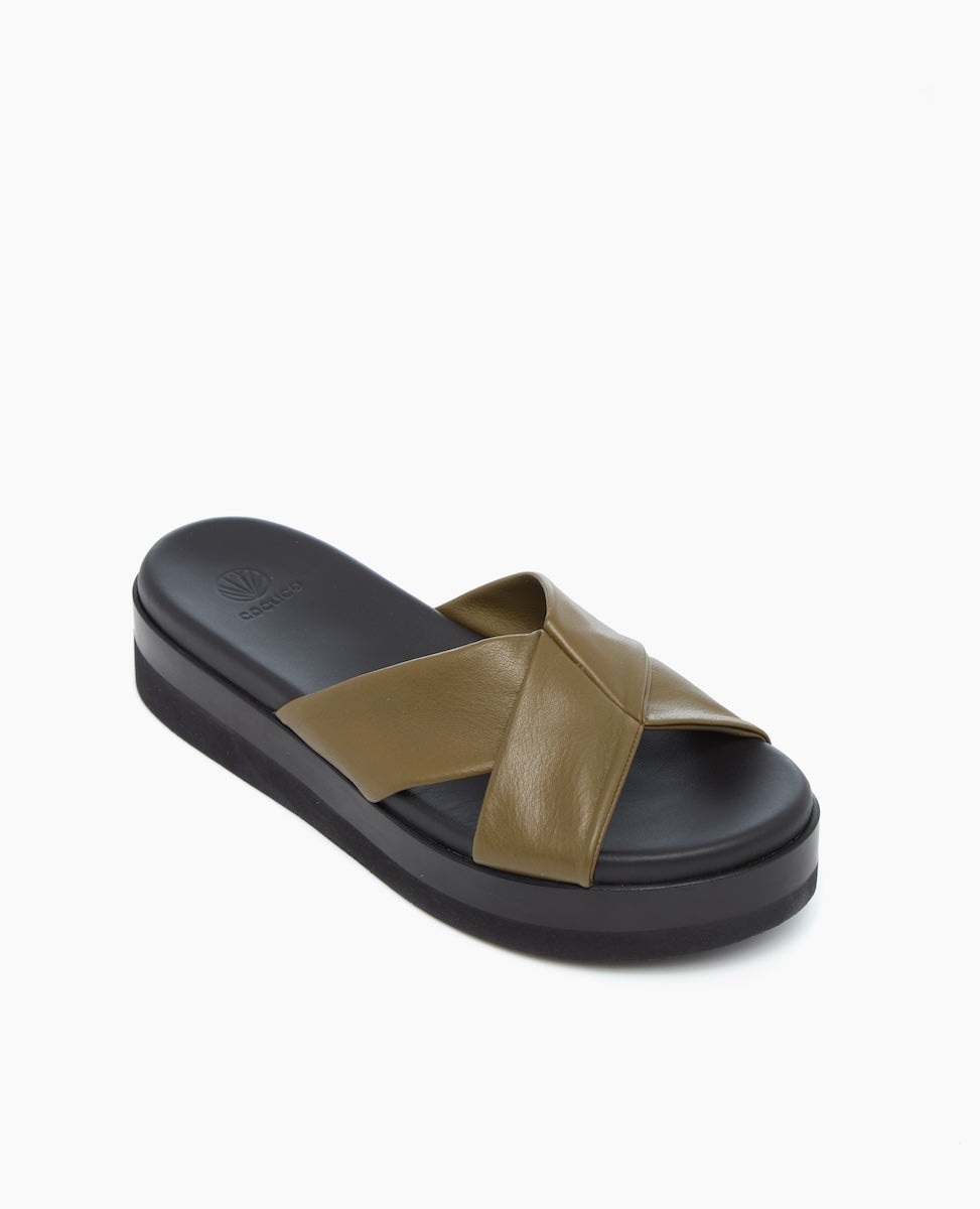 A sandal featuring a thick black platform sole and a wide, olive green leather strap that crosses over the top in an X shape.