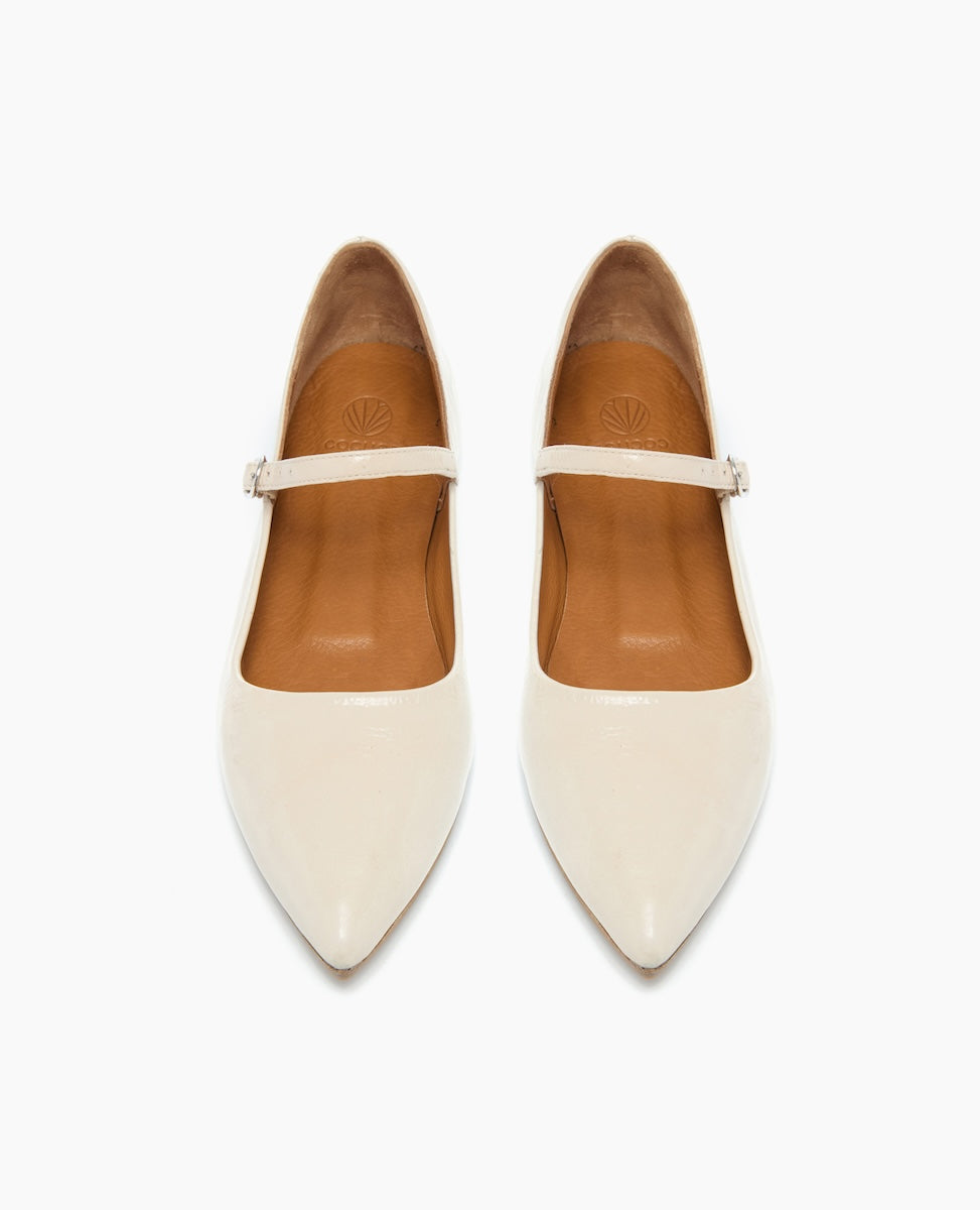 Cream-colored, pointed-toe flats with a glossy finish, featuring a single thin strap across the top and a tan interior lining.