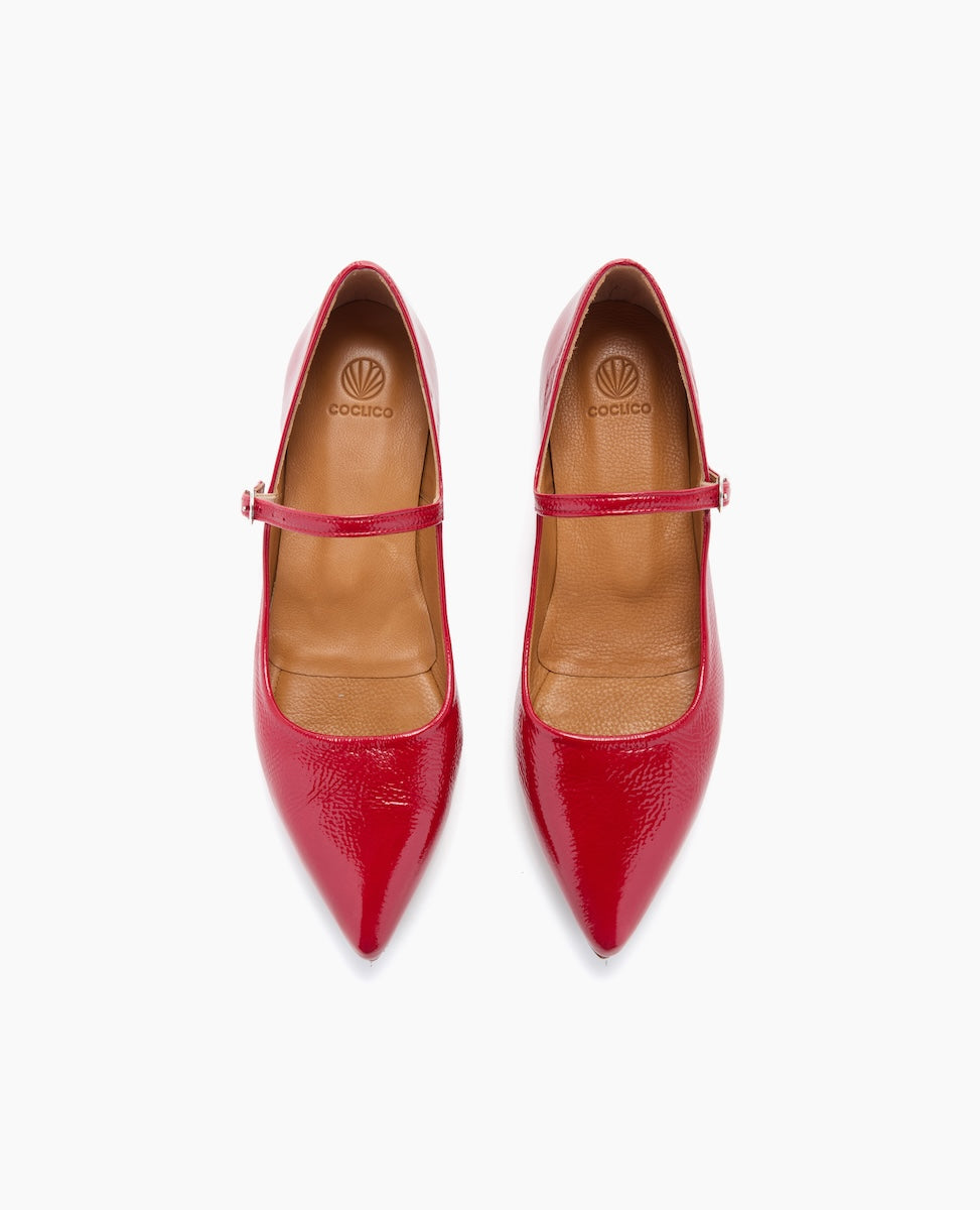 A pair of glossy red patent leather Mary Jane shoes with pointed toes, a single thin strap across the instep, and a tan leather interior featuring a logo on the insole.