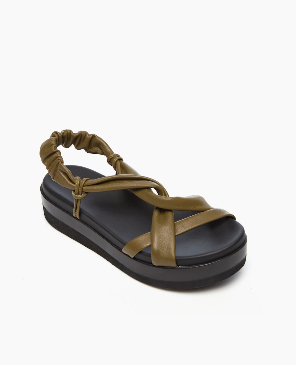 A sandal featuring a thick black platform sole, olive green leather straps with a crisscross design, and an elasticized back strap for a secure fit.