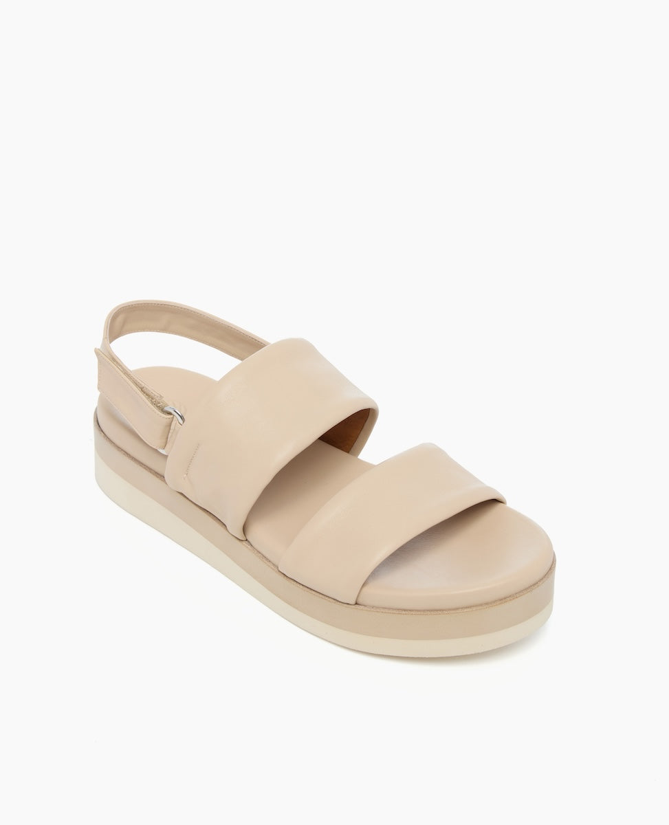 A beige sandal with a thick platform sole, featuring two wide straps across the top and a slingback strap, made of smooth leather material.