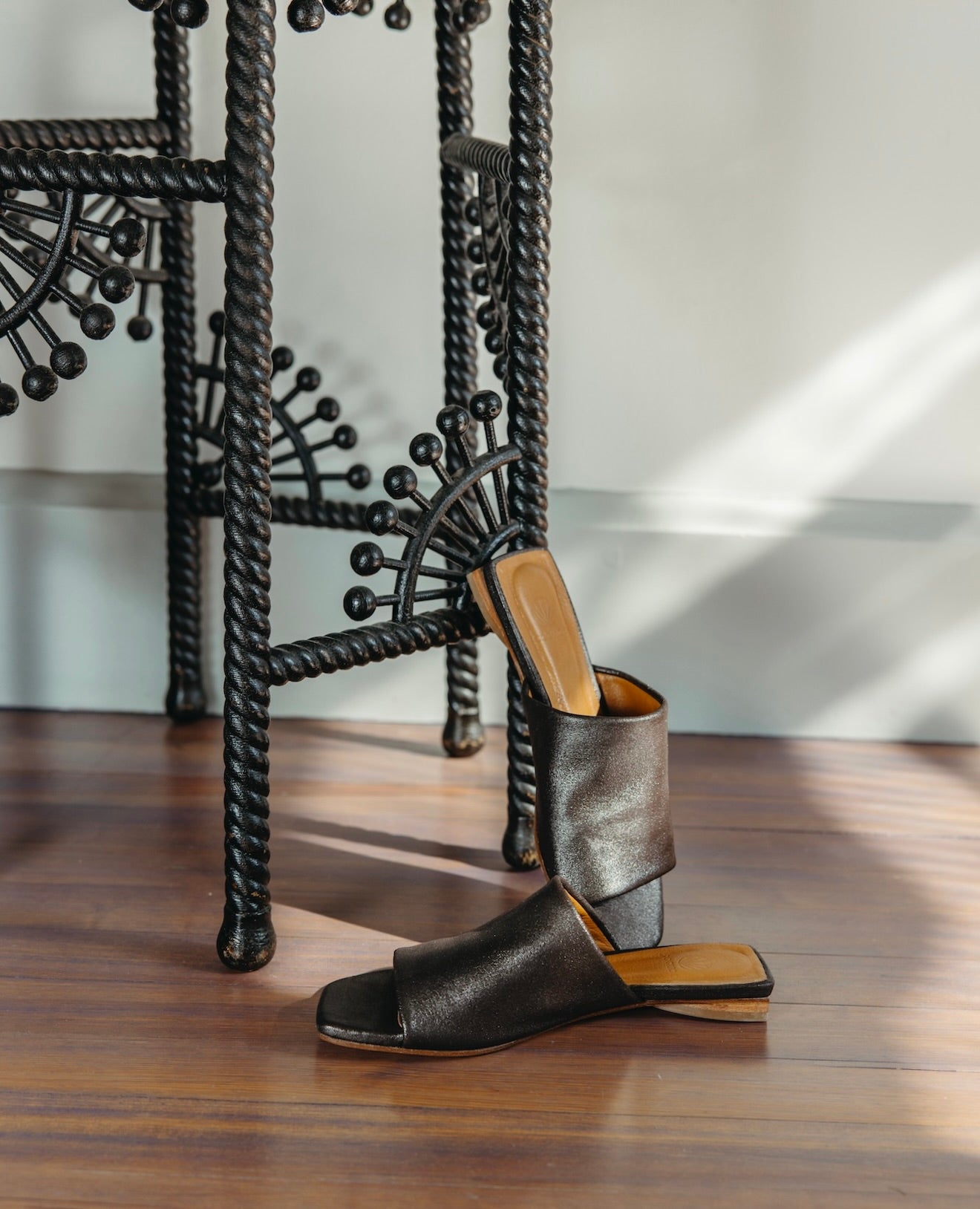 Ferhana Sandal in anthracite shimmer suede with the left sandal propped up against a black night table.