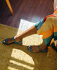 Legs stretched out against a yellow rug with a rainbow dress stretched over the knees and wearing the Fifi Sandal in Cerulean. 7