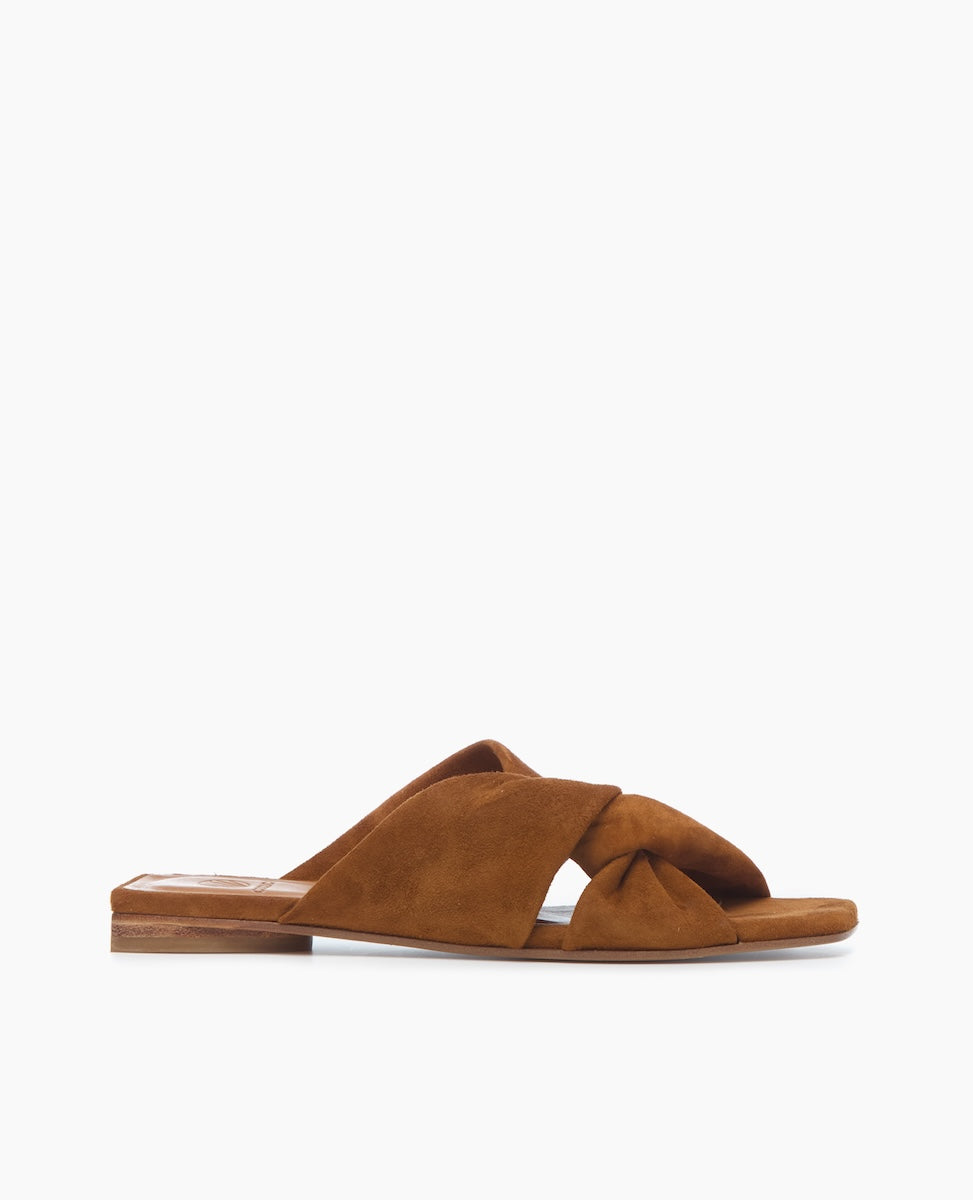 A brown suede sandal featuring a flat sole, crisscross straps with a knot detail, and a minimalist design.